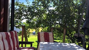 Uma área de estar confortável ao ar livre, com sofá e poltronas, uma mesa e vista para uma árvore e um campo gramado.