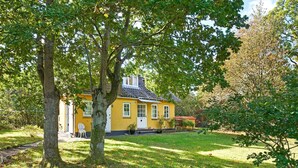 A yellow house with a white door and windows, surrounded by trees and grass. - 5 Person Holiday Home in Nexo-by Traum (Nexø)