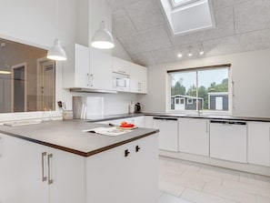 A modern kitchen with white cabinetry, a central island, pendant lighting, and a view of a house through a window.