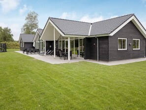 A modern building with a covered patio area, a lawn, and a clear sky. - 5 Star Holiday Home in Vaeggerlose (Vaeggerlose)