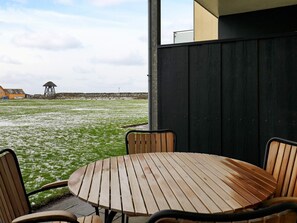 A round wooden table with four chairs, a black metal fence, and a grassy area with a stone wall in the background. - 4 Person Holiday Home in Lokken (Lokken)
