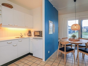A kitchen with white cabinets, a coffee maker, a toaster, and a dining area with a table and chairs. - 4 Person Holiday Home in Lokken (Lokken)