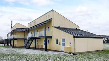 A two-story building with a flat roof, a staircase leading to the upper floor, and a small fenced area in front.