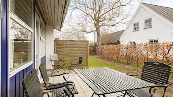 Un patio al aire libre con una mesa y cuatro sillas, una cerca de madera y una casa al fondo.