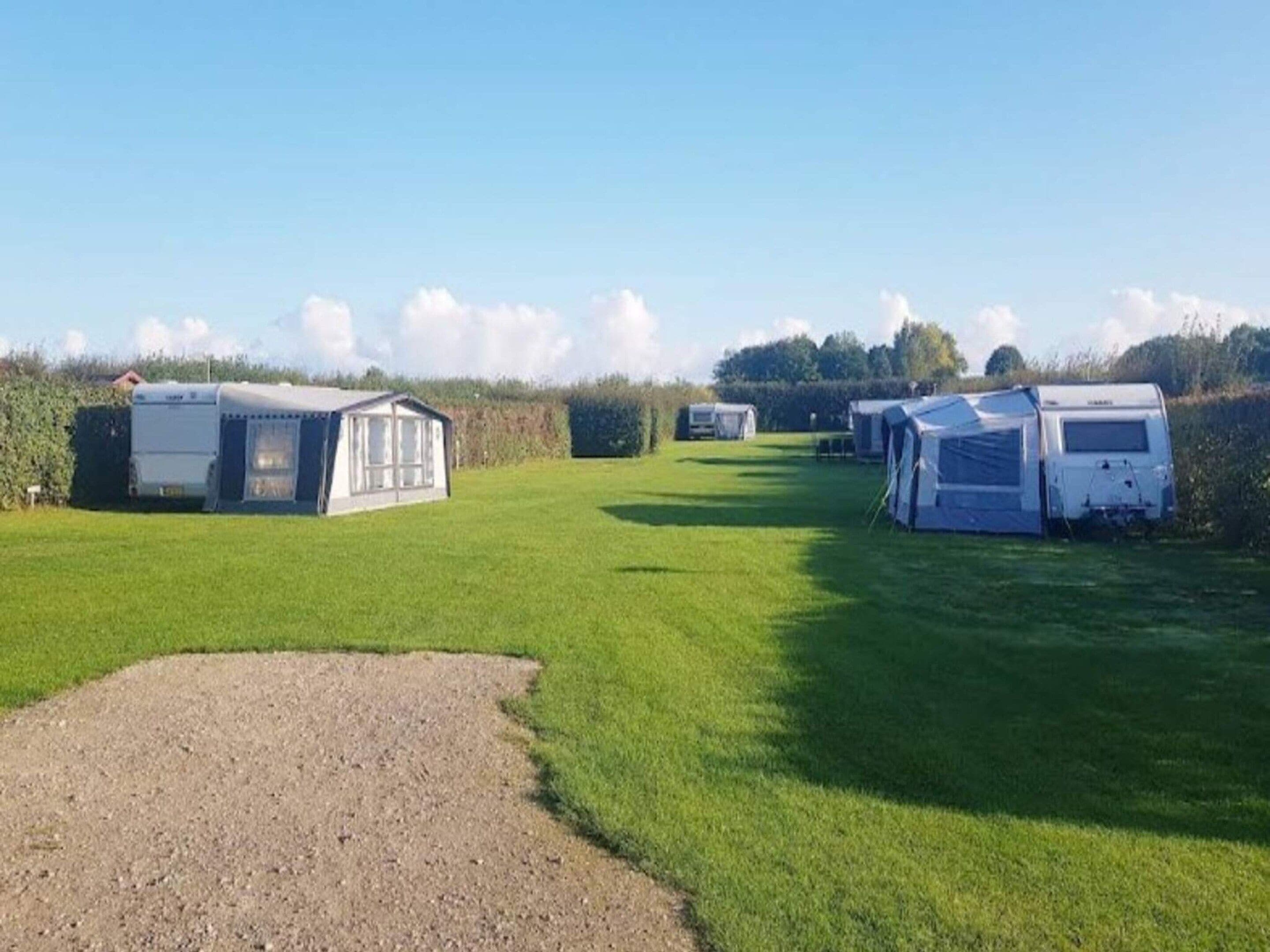 A campsite with several caravans and a small building, likely a communal area, set in a grassy field with a clear sky.