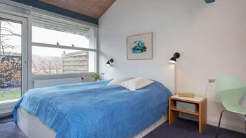 A bedroom with a large bed, a nightstand, a chair, a window with a view, and a painting on the wall.