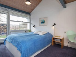 Et soveværelse med en stor seng, et vindue, et natbord, en stol og et billede på væggen.