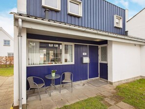 Un immeuble résidentiel à la façade bleue, avec une porte d’entrée et un petit patio comprenant deux chaises et une table.
