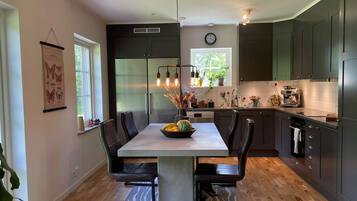 Una cocina moderna con una isla central, armarios oscuros y un comedor con una mesa grande y sillas.
