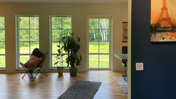 A spacious room with large windows, a chair, a potted plant, and a painting of the Eiffel Tower. - 5 Star Holiday Home in Klovedal (Klovedal)