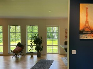 A spacious room with large windows, a chair, a potted plant, and a painting of the Eiffel Tower. - 5 Star Holiday Home in Klovedal (Klovedal)