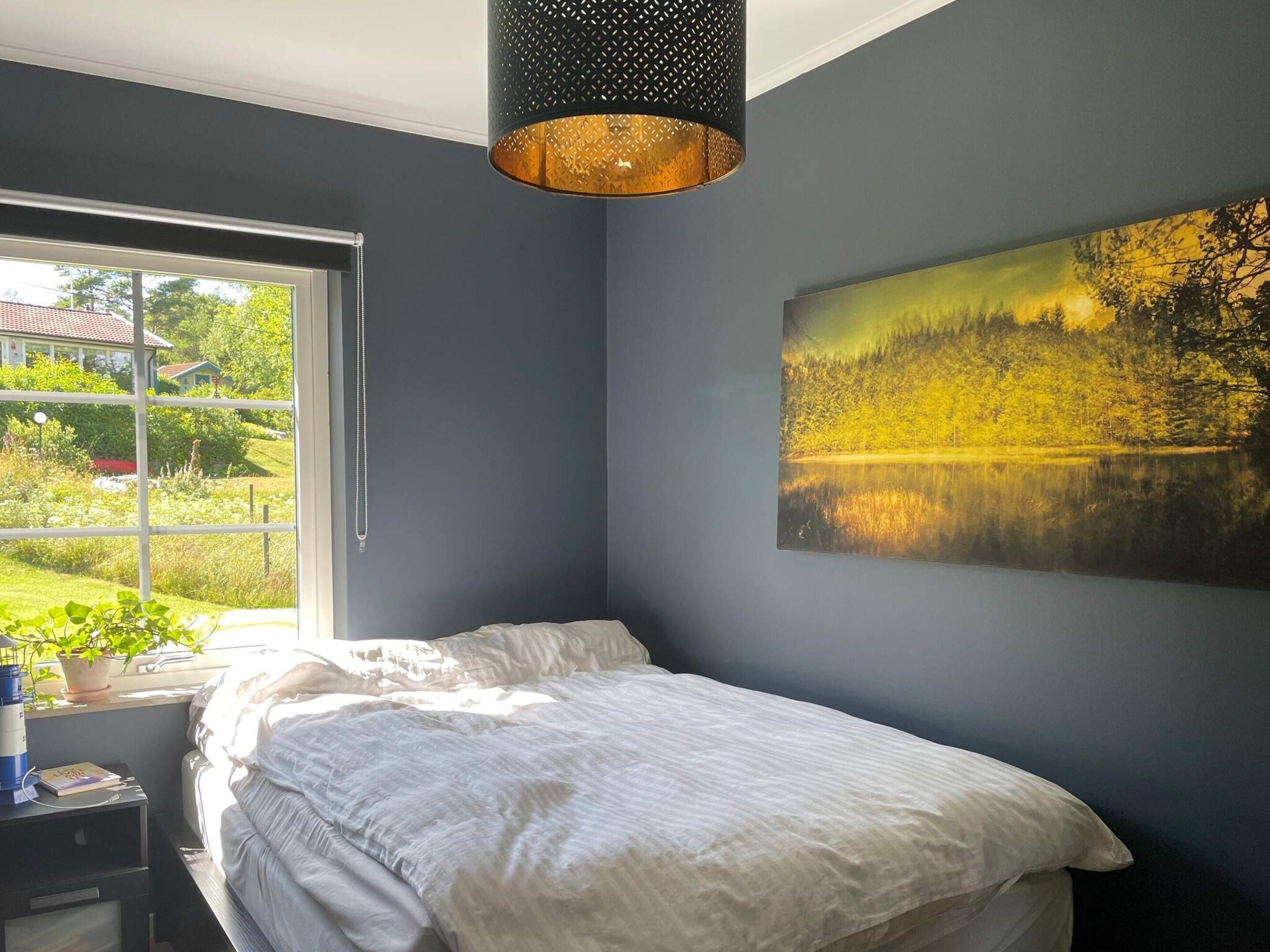 Et soveværelse med en seng, et vindue, et billede og en hængende lampe.