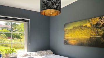 Et soveværelse med en seng, et vindue, et billede og en hængende lampe.