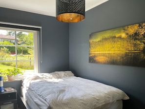 A bedroom with a bed, a window, a painting, and a hanging light fixture.