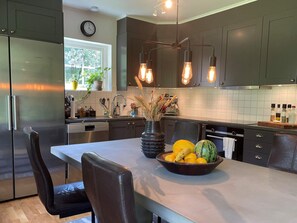 A modern kitchen with stainless steel appliances, a central island with a fruit bowl, and pendant lighting.