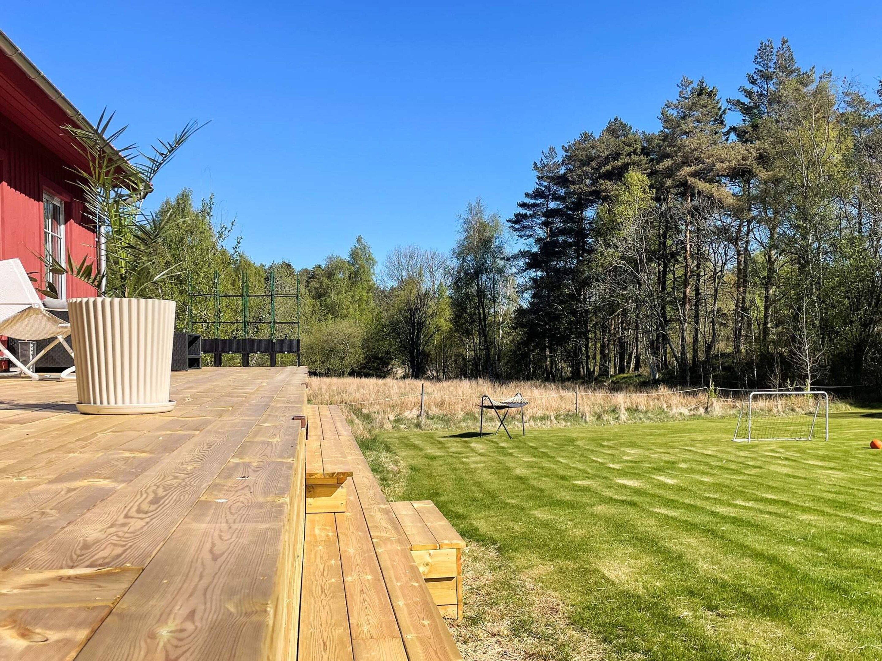 Een houten terras met een rood gebouw op de achtergrond, een gazon en een tennisbaan.
