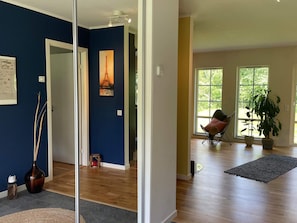 A spacious room with hardwood flooring, a large window with a view of greenery, and a chair with a cushion.