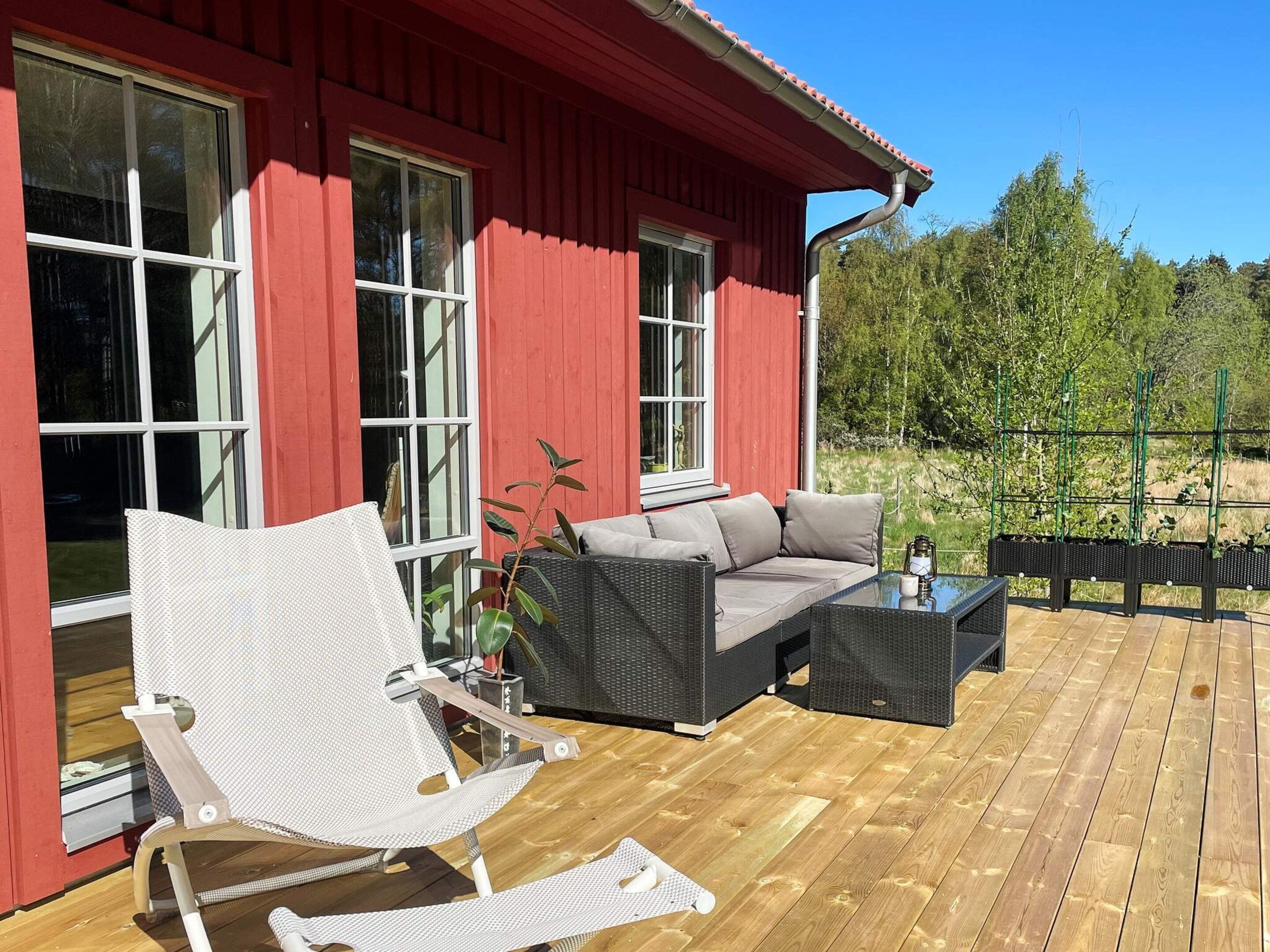 A red building with large windows, a wooden deck, a wicker sofa, a white chair, and a small table.