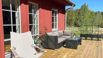 Ein rotes Gebäude mit großen Fenstern, einer Holzterrasse, einem Korbsessel, einem weißen Stuhl und einem kleinen Tisch.