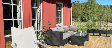 A red building with large windows, a wooden deck, a wicker sofa, a white chair, and a small table.