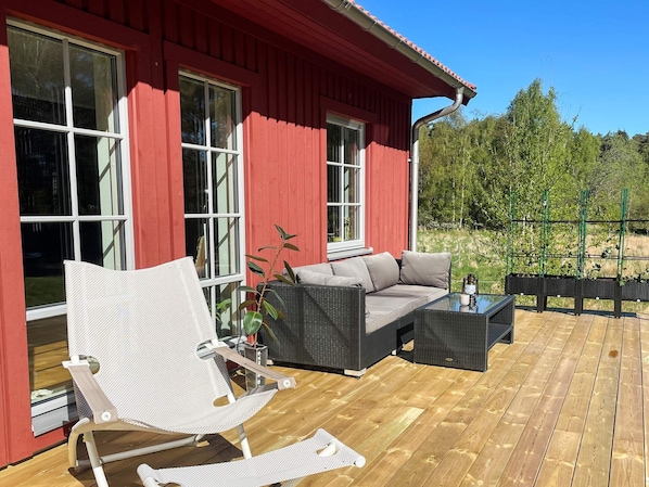 A red building with large windows, a wooden deck, a wicker sofa, a white chair, and a small table.