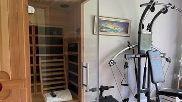 Eine Sauna mit einer Bank und einer Glastür, einem an der Wand befestigten Trainingsgerät und einem gerahmten Gemälde.