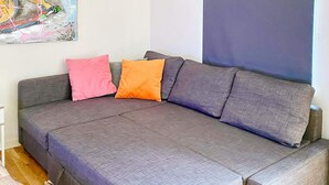 A grey sofa with a pull-out bed, a pink and orange pillow, and a large abstract painting on the wall. - 5 Star Holiday Home in Klovedal (Klovedal)