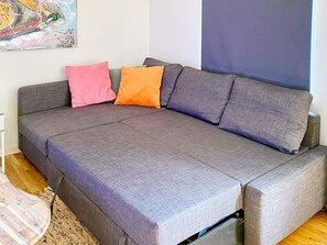 A grey sofa with a pull-out bed, a pink and orange pillow, and a large abstract painting on the wall.