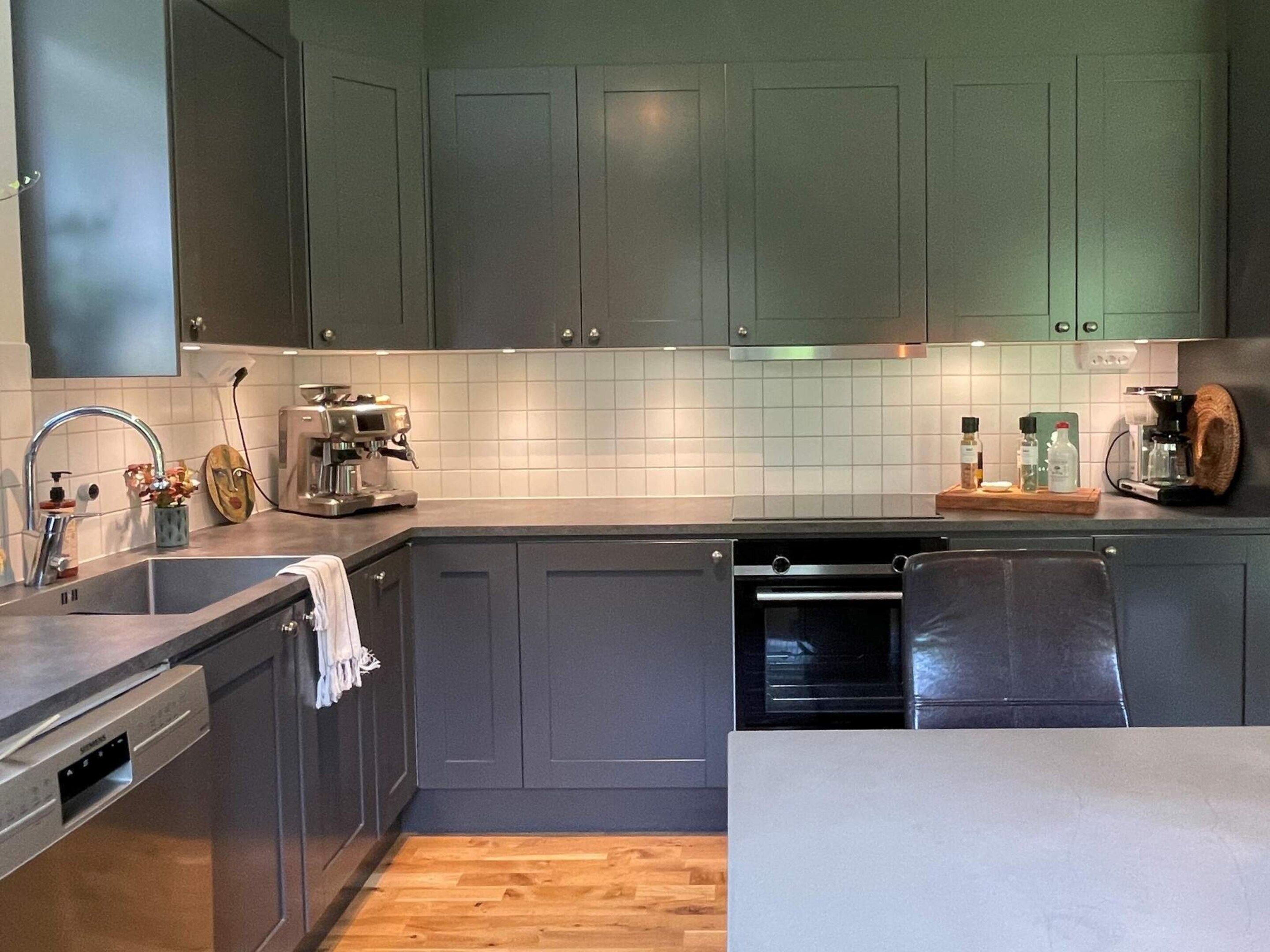 A modern kitchen with grey cabinets, a stainless steel sink, a coffee machine, and a wooden countertop.