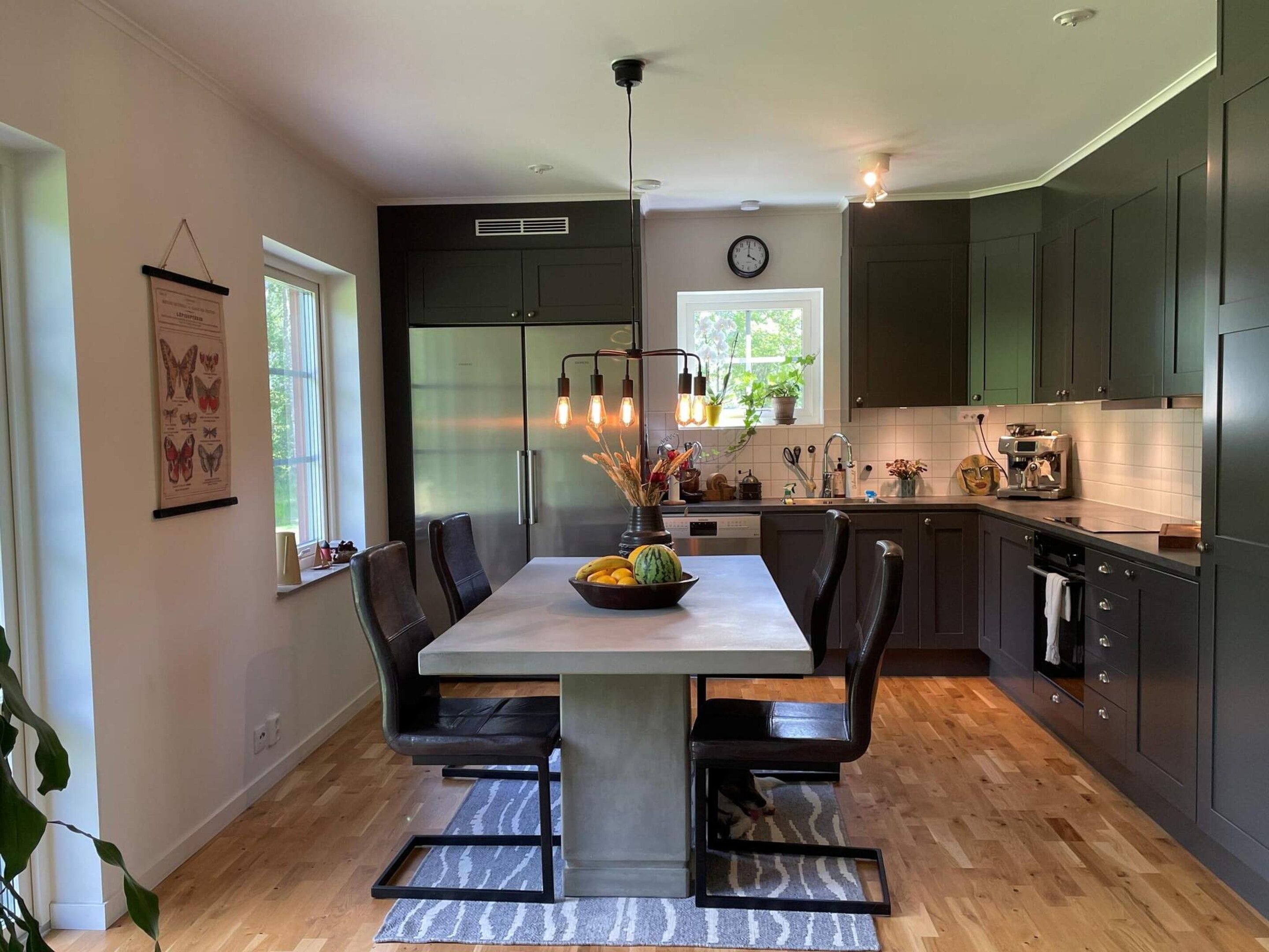 A modern kitchen with dark cabinets, a stainless steel refrigerator, and a dining area with a table and chairs.
