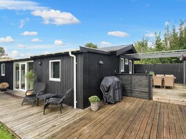 Una terraza de madera oscura con mobiliario exterior, una parrilla y un pérgola.