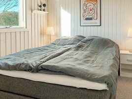 Een slaapkamer met een bed, nachtlampjes, een raam en een kunstwerk in een lijst aan de muur.