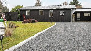 Rakennus, jonka edessä on sorapäällysteinen ajotie, pieni nurmikko ja taustalla puinen aita.