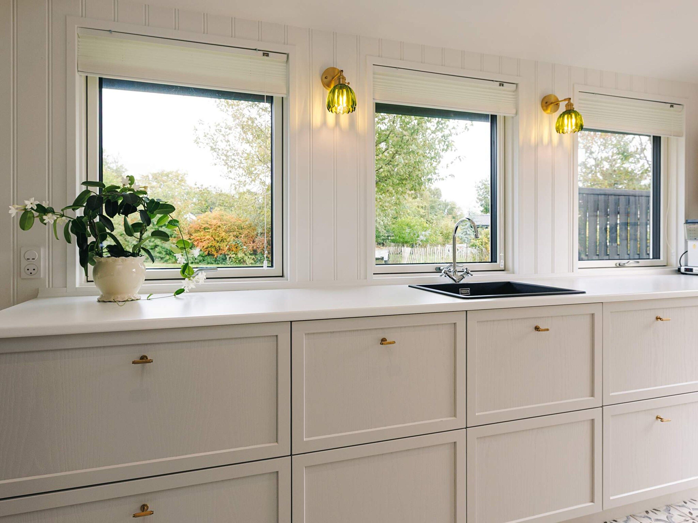 A kitchen with white cabinetry, a black sink, and three windows with light fixtures.