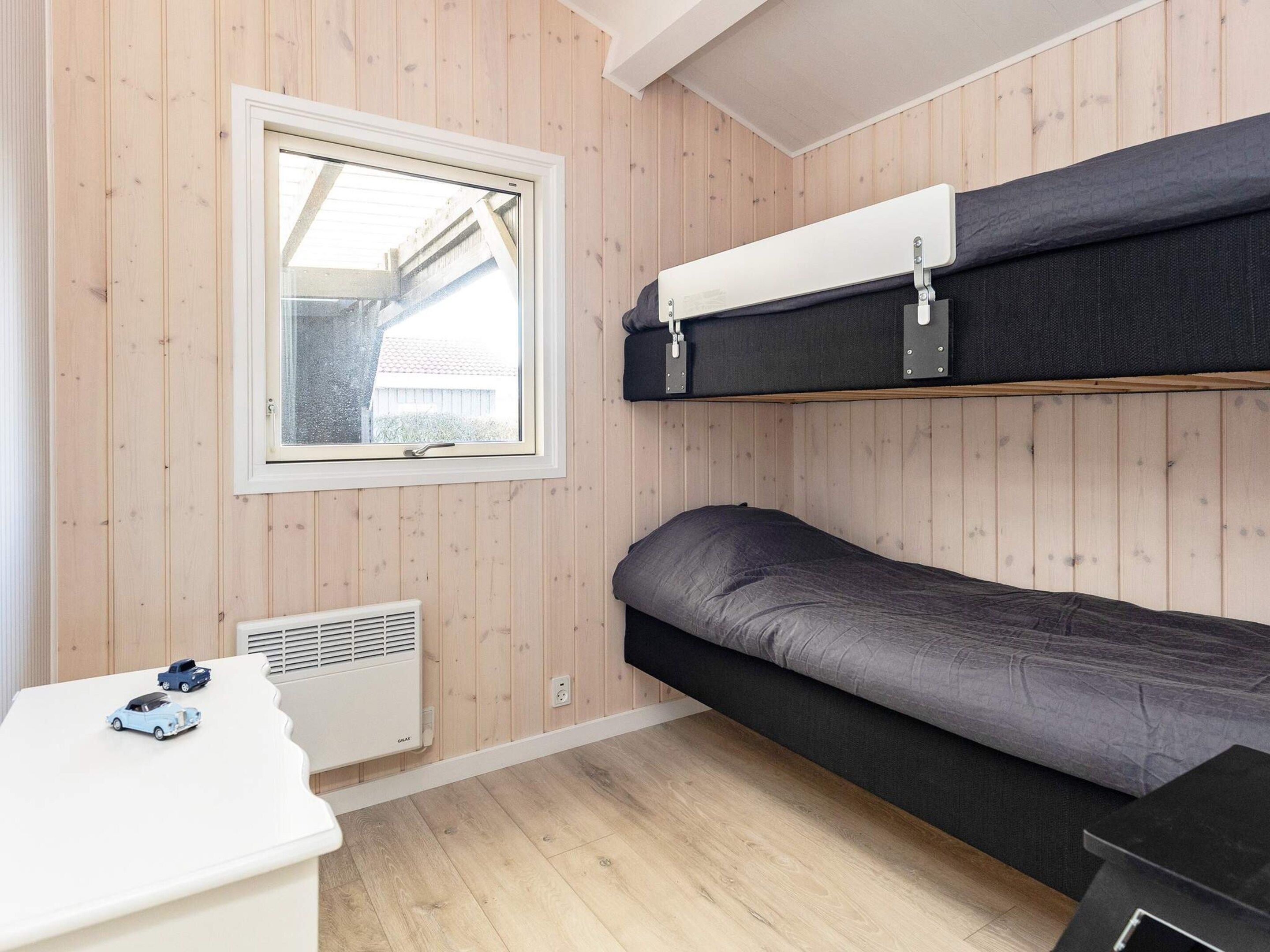 Ein kleines Zimmer mit Etagenbett, einem Tisch mit Spielzeug, einem Fenster und einer Heizung.