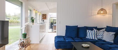 A modern living room with a blue sofa, a black coffee table, and a TV on the left.