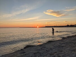 Een strandscène met een ondergaande zon, rustig water en een persoon die in het water staat.