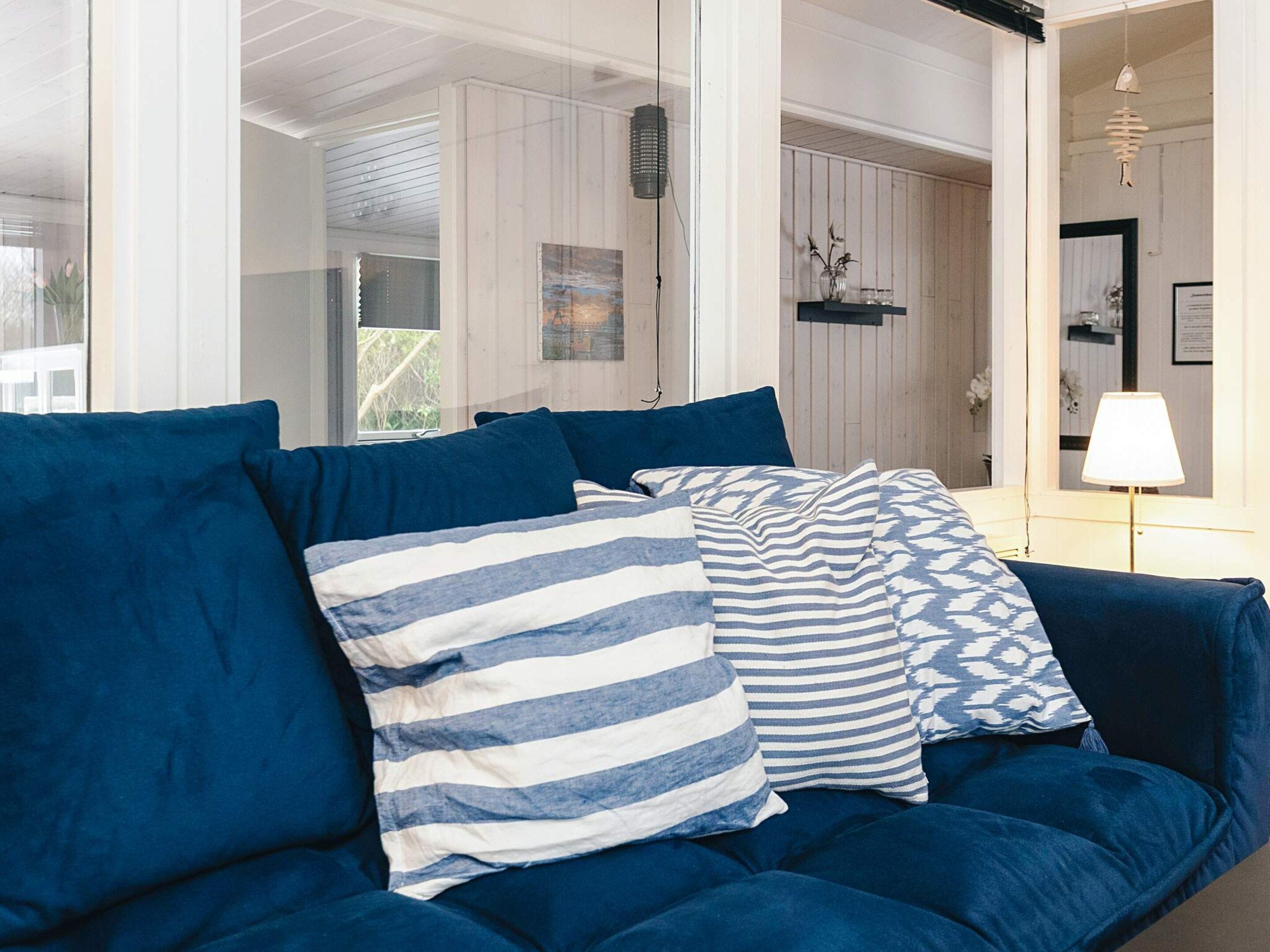 A blue sofa with striped and patterned cushions in a room with wooden walls and a hanging lamp.