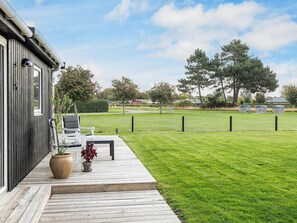A wooden deck with outdoor seating, a lawn, and a fenced area with trees. - 4 Star Holiday Home in Karrebaeksminde (Karrebæksminde)