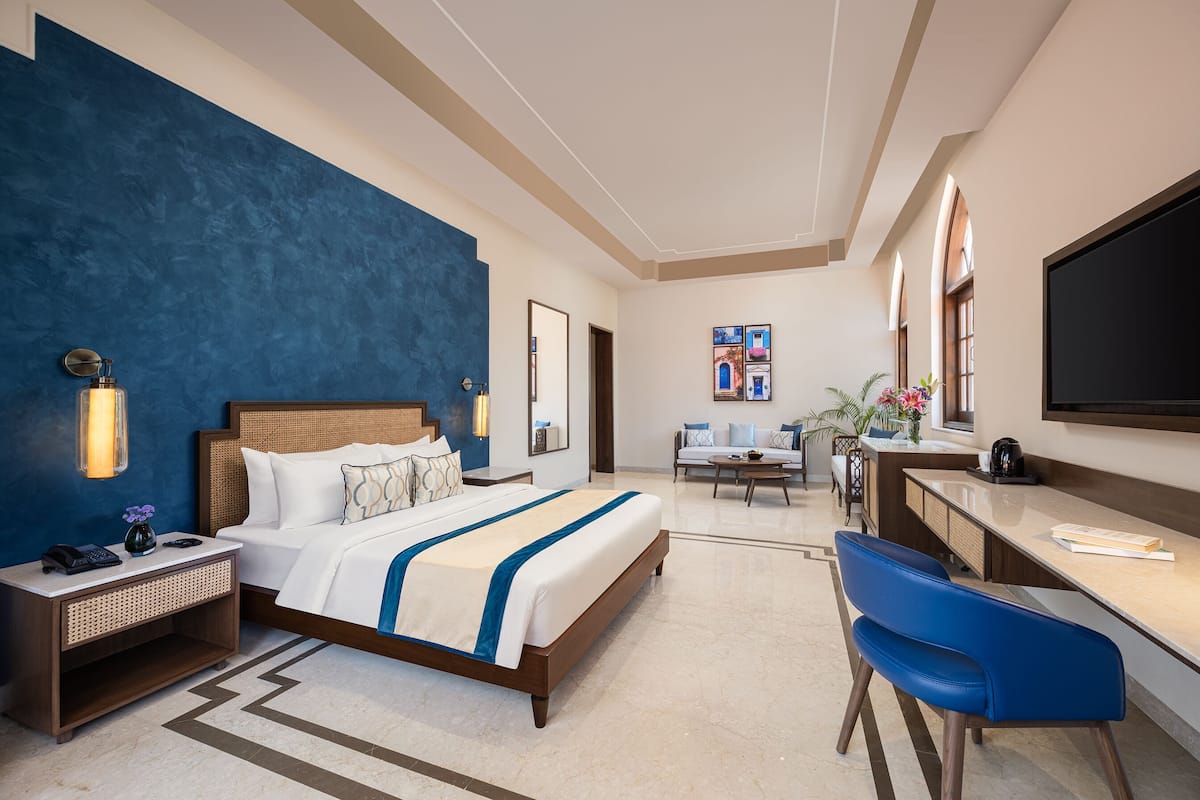 A hotel room with a bed, bedside table, desk, chair, and a TV.