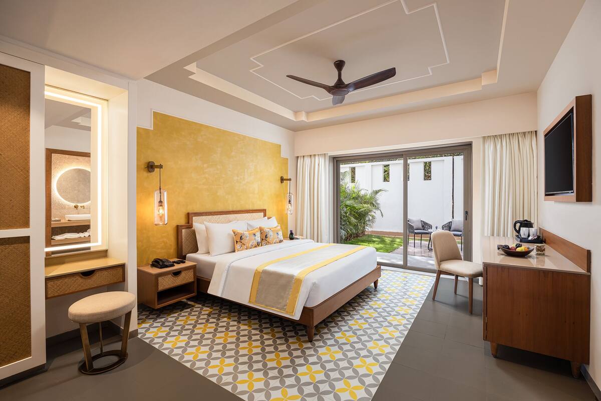 A hotel room with a bed, a desk, a chair, a TV, and a balcony with a view of the outside.
