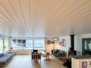 Een moderne woonkamer met een bank, stoelen, een tafel, een open haard en grote ramen.
