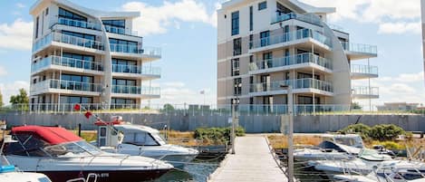 En småbåtshamn med moderna lägenhetsbyggnader, förtöjda båtar och en träpromenad.
