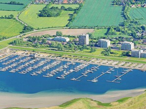 Vista aérea de uma marina com diversos barcos atracados, cercada por edifícios residenciais e campos verdes.