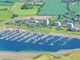 Vista aérea de un puerto deportivo con numerosas embarcaciones amarradas, rodeado de edificios residenciales y campos verdes.