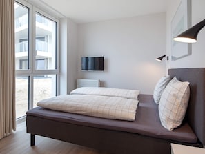 A modern bedroom with a bed, a television, and a window with curtains.