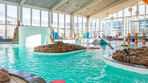 Une piscine intérieure à l’eau claire, dotée de plusieurs couloirs de nage et de diverses structures de jeux colorées.