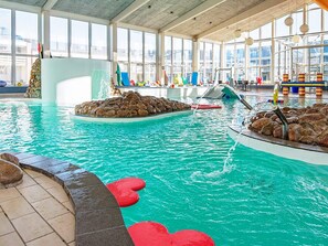 Une piscine intérieure à l’eau claire, dotée de plusieurs couloirs de nage et de diverses structures de jeux colorées.