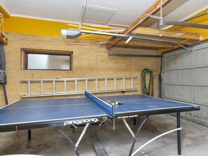 Ett bordtennisbord i ett rum med en tegelvägg, ett fönster och en garageport.