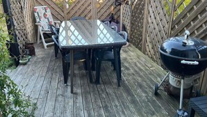 Une terrasse en bois avec une table et des chaises à plateau en verre, un barbecue et une clôture en bois.